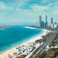 Aerial view of Abu Dhabi with high-rise buildings, a long sandy beach, and blue water under a clear sky.