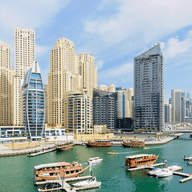Panoramic view of Dubai Marina with modern skyscrapers, boats docked in the harbor, and clear blue skies.