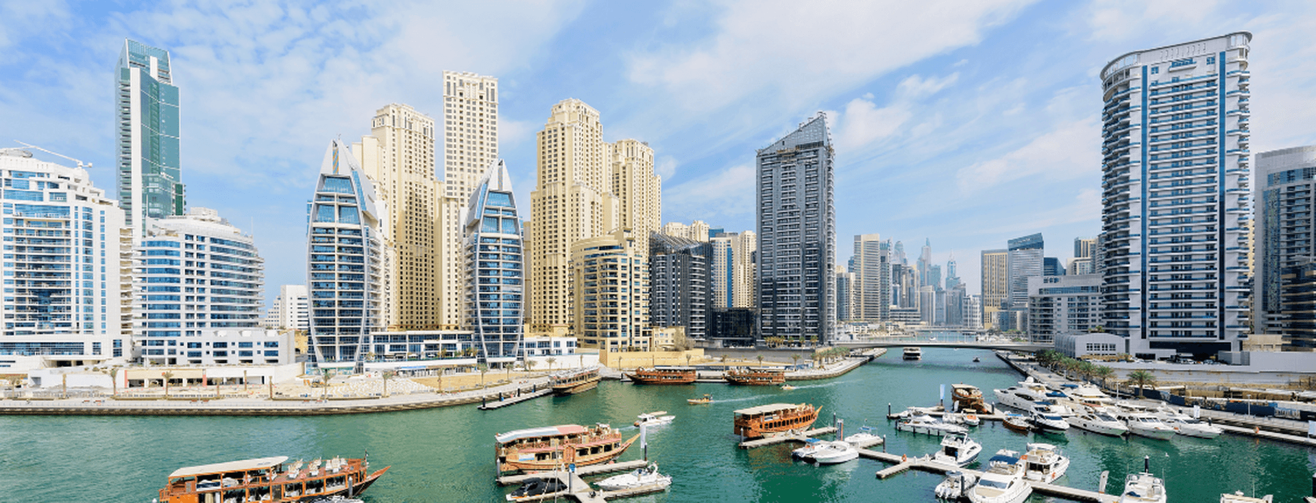 Panoramic view of Dubai Marina with modern skyscrapers, boats docked in the harbor, and clear blue skies.