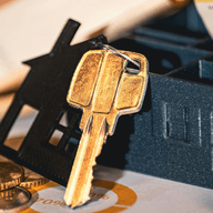 Foto zeigt einen Schlüsselhalter in Form eines schwarzen Hauses mit einem goldenen Schlüssel, Münzen und Bargeld