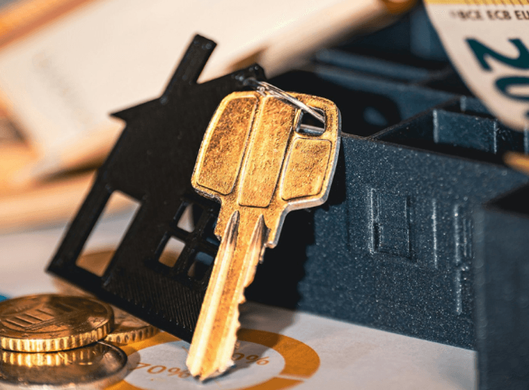 Foto zeigt einen Schlüsselhalter in Form eines schwarzen Hauses mit einem goldenen Schlüssel, Münzen und Bargeld