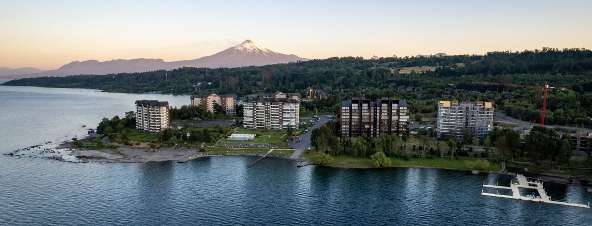 Vista aérea de condominios junto al lago con una montaña nevada al fondo.