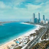 Aerial view of Abu Dhabi with high-rise buildings, a long sandy beach, and blue water under a clear sky.