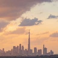 Skyline of Dubai at sunset with Burj Khalifa, scattered clouds, and a warm, colorful sky.