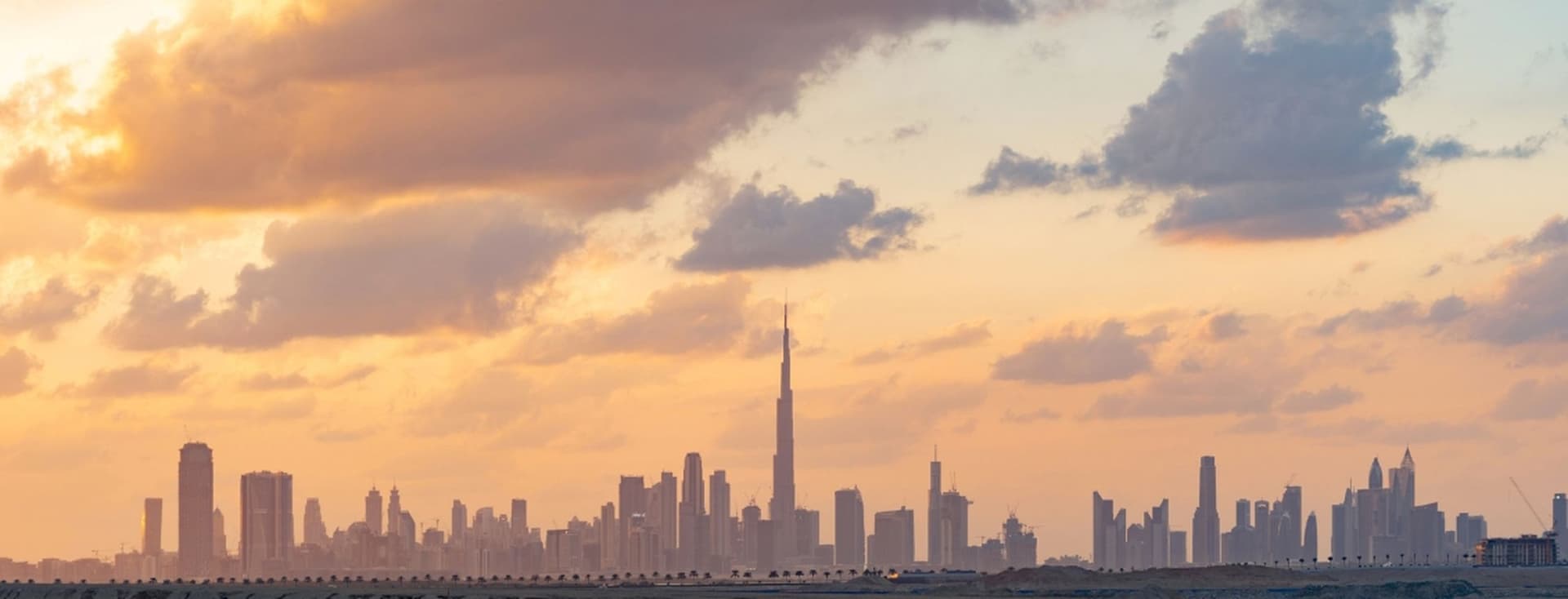 Skyline of Dubai at sunset with Burj Khalifa, scattered clouds, and a warm, colorful sky.