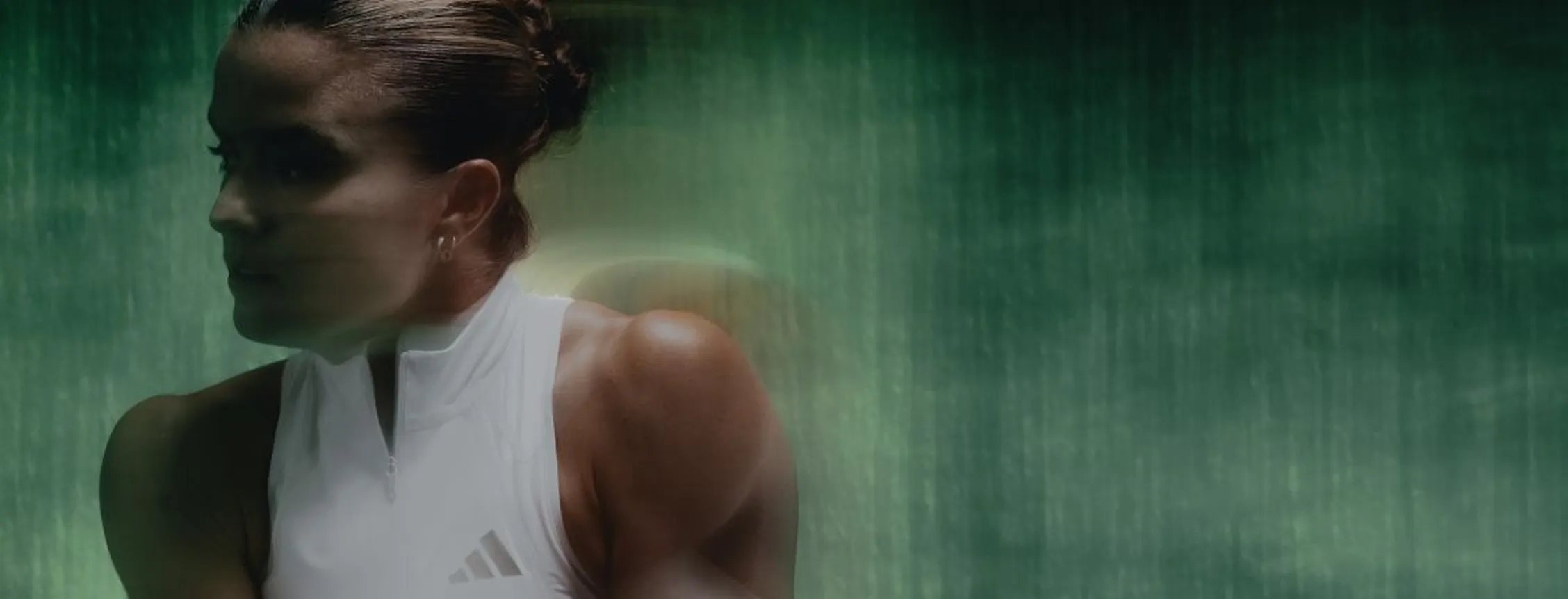 Intense side-profile shot of tennis player Maria Sakkari focused during movement against a dark textured background.