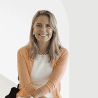 A smiling woman with blonde hair wearing a white dress and orange cardigan.