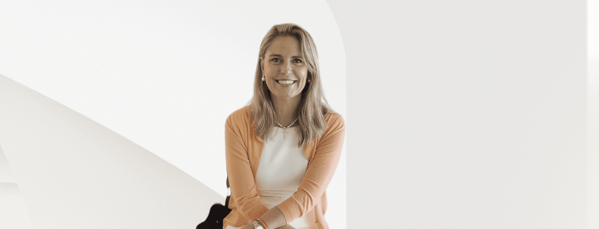 Una dona somrient amb cabells rossos que porta un vestit blanc i un cardigan taronja.