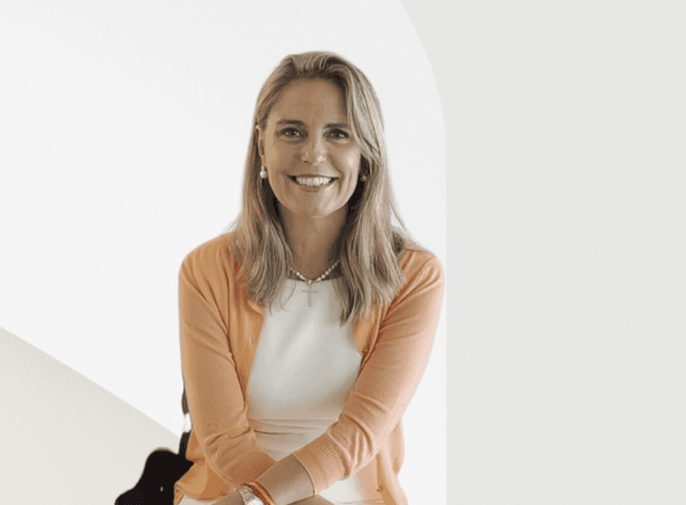 Una dona somrient amb cabells rossos que porta un vestit blanc i un cardigan taronja.