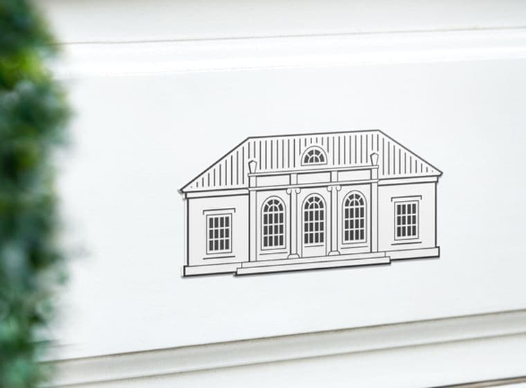 Engel & Völkers Villa Logo auf einer weißen Wand. Auf der linken Seite ist leicht verschwommen ein grüner Buchsbaum.