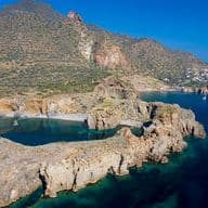 Luftaufnahme einer zerklüfteten Küste mit felsigen Klippen, klarem blauem Wasser und einer entfernten Küstenstadt unter klarem Himmel.