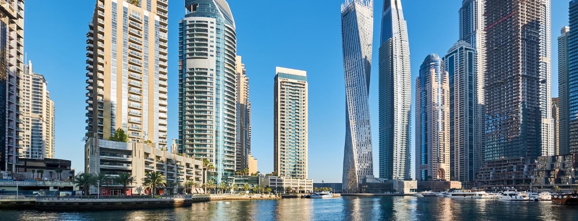 Skyline of modern skyscrapers reflecting in the water, under a clear blue sky, with a mix of unique architectural designs.