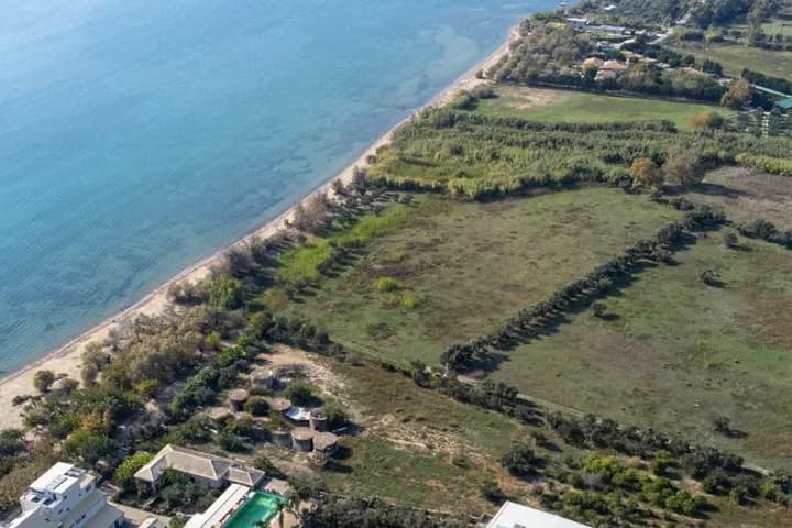 Aerial view of a large beachfront plot of land along a sandy coastline with clear blue sea.