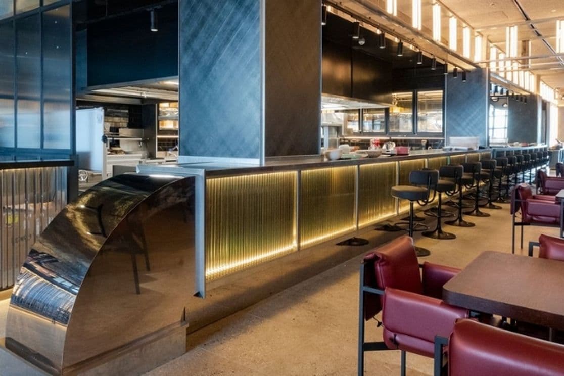 Modern restaurant interior with a sleek bar, high chairs, red cushioned seating, and ambient lighting, creating a cozy atmosphere.