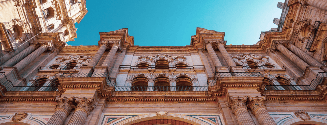 A large part of the front façade of Málaga Cathedral seen from below, with a clear blue sky in the background.