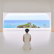 Eine Person in einem weißen Kleid kniet in einem minimalistisch gestalteten weißen Raum und blickt durch ein großes Bogenfenster auf das Meer.