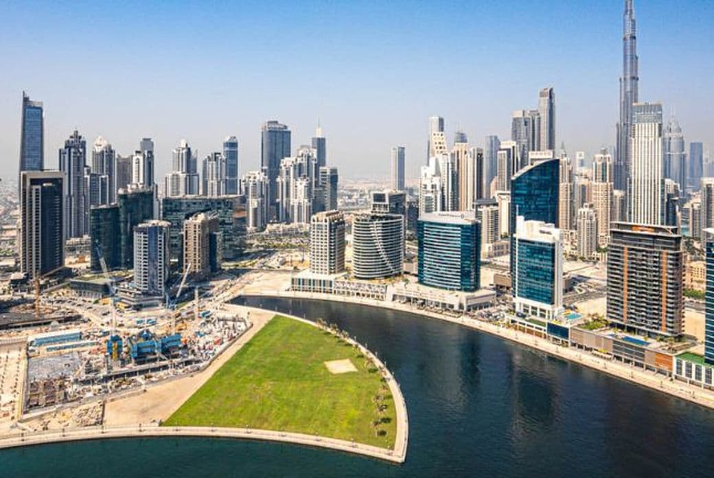 Aerial view of a Business Bay Canal featuring numerous skyscrapers alongside a winding waterfront under a clear blue sky.