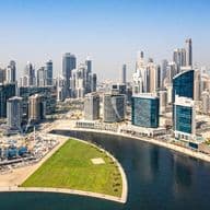 Luftaufnahme eines Kanals in Business Bay mit zahlreichen Wolkenkratzern entlang der geschwungenen Uferpromenade unter klarem blauem Himmel.