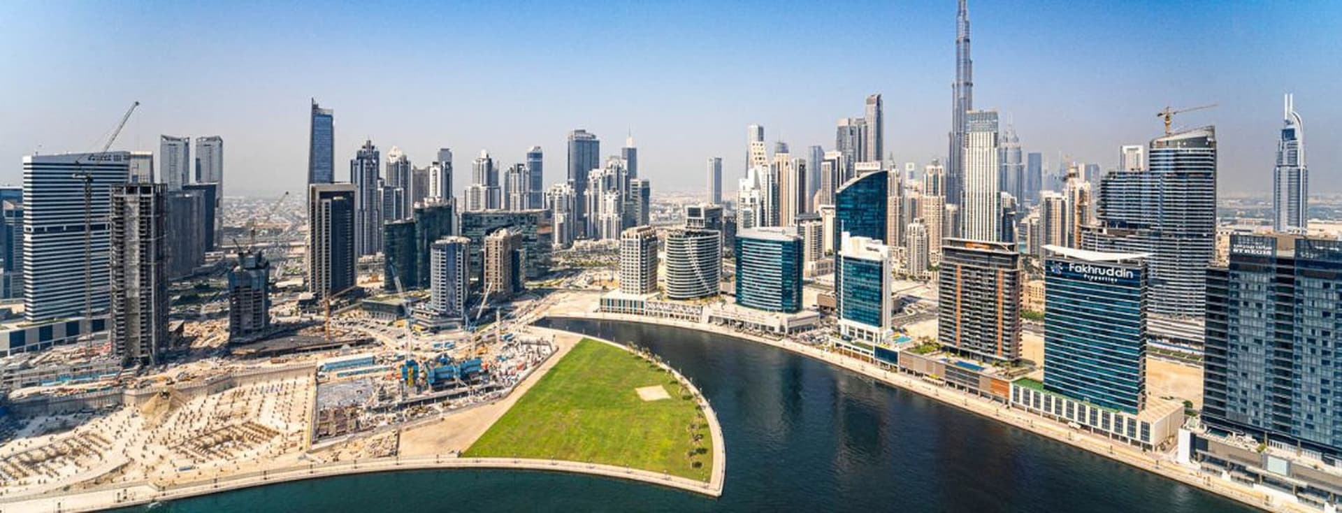 Aerial view of a Business Bay Canal featuring numerous skyscrapers alongside a winding waterfront under a clear blue sky.