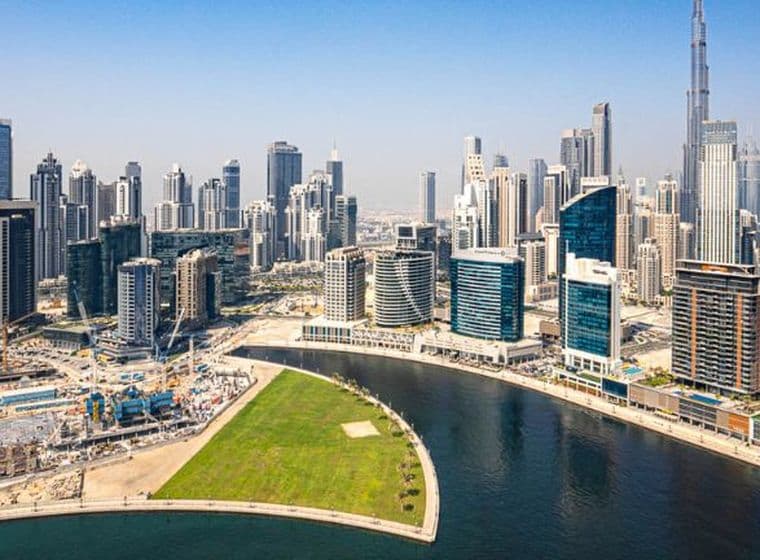 Luftaufnahme eines Kanals in Business Bay mit zahlreichen Wolkenkratzern entlang der geschwungenen Uferpromenade unter klarem blauem Himmel.