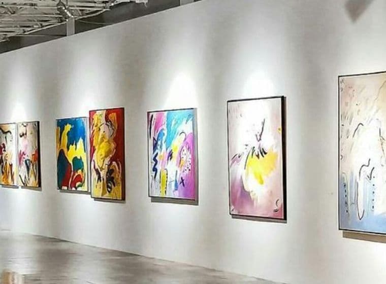 Kunstgalerie mit Besuchern, die farbenfrohe abstrakte Gemälde an weißen Wänden unter heller Beleuchtung betrachten.