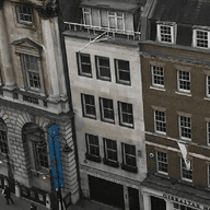 Straßenansicht von Londoner Gebäuden mit Menschen, die auf dem Bürgersteig gehen. Die Gebäude sind grau, weiß, braun und rot.