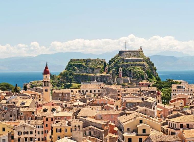 Panoramic view of a coastal town with historic buildings, sea, and hilltop fortress