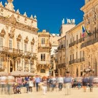 Piazza Duomo in Ortigia, Syrakus, mit eleganten barocken Gebäuden, flanierenden Menschen und einem strahlend blauen Himmel.