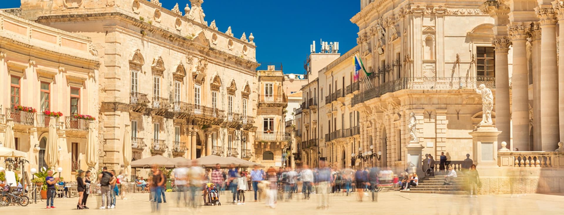 Piazza Duomo in Ortigia, Syrakus, mit eleganten barocken Gebäuden, flanierenden Menschen und einem strahlend blauen Himmel.
