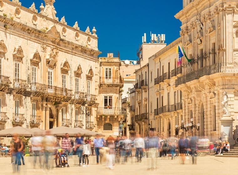 Piazza Duomo in Ortigia, Syrakus, mit eleganten barocken Gebäuden, flanierenden Menschen und einem strahlend blauen Himmel.