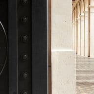 Gros plan sur un grand porte d'entrée à gauche, avec en arrière-plan un couloir à colonnes au sol carrelé et décoré à droite.