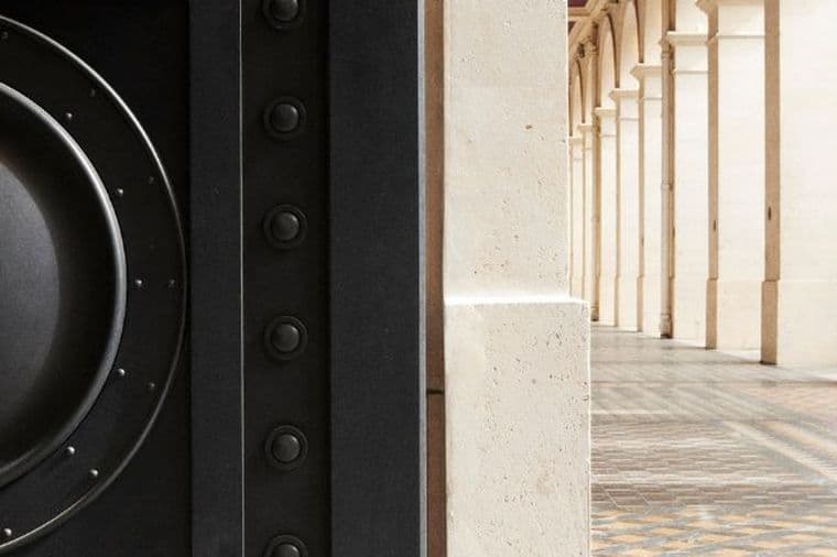 Close-up of a large speaker on the left, with a background of a columned hallway featuring ornate tiled flooring on the right.