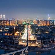 Panoramic view of Dubai at night, featuring illuminated skyscrapers, a lit bridge, and reflections on the water.
