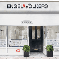 Engel & Völkers real estate office exterior. White building with black trim, awning, and "Great Place to Work" certification.