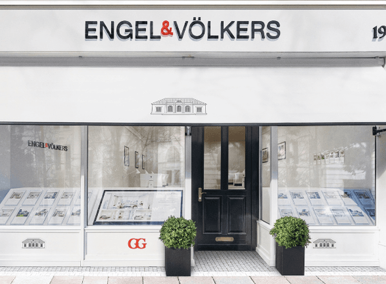 Oficina immobiliària d'Engel & Völkers a l'exterior. Edifici blanc amb detalls en negre, tendal i certificació de "Great Place to Work".