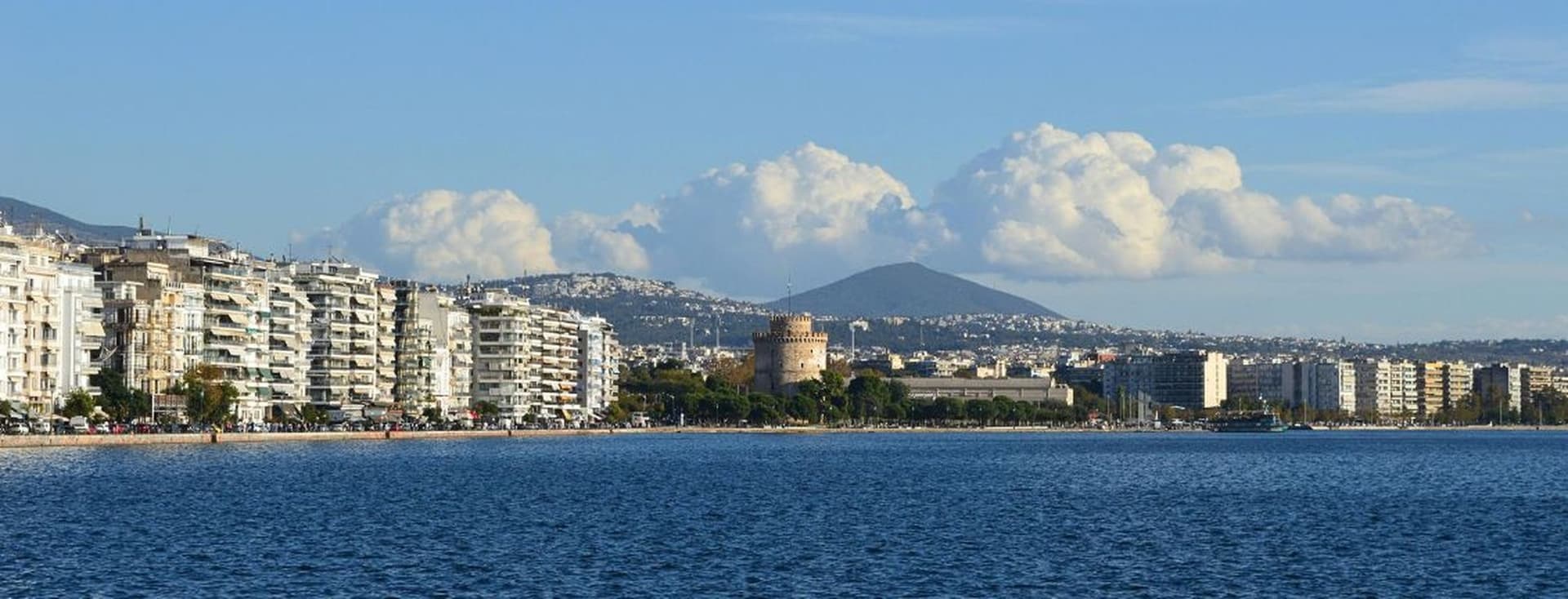 Seafront view of Thessaloniki with White Tower, waterfront buildings, and mountain backdrop