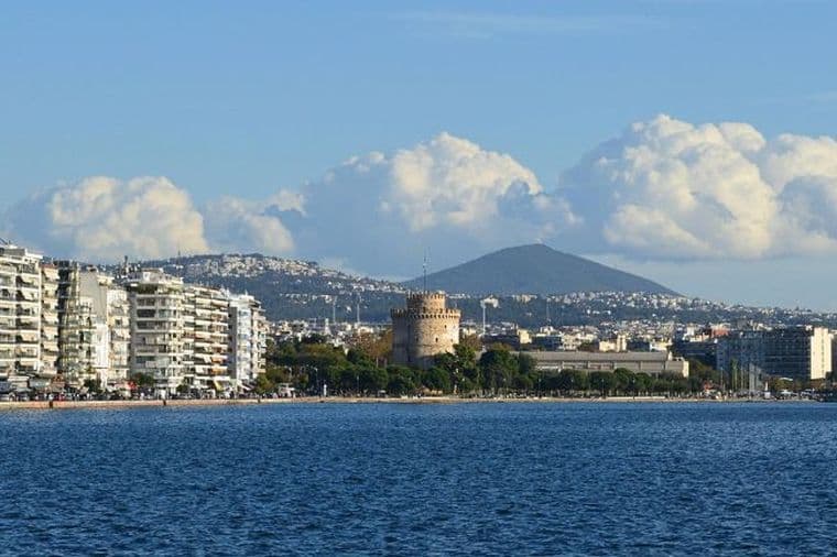 Seafront view of Thessaloniki with White Tower, waterfront buildings, and mountain backdrop