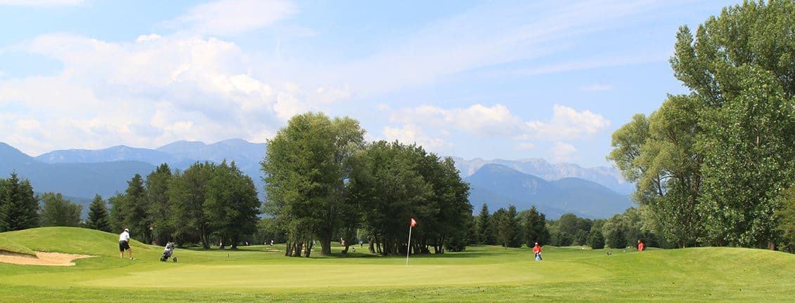 camp de golf amb jugadors envoltat d'arbres i vistes a les muntanyes.
