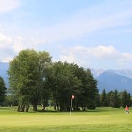 Golfplatz mit Spielern, umgeben von Bäumen und mit Blick auf die Berge.