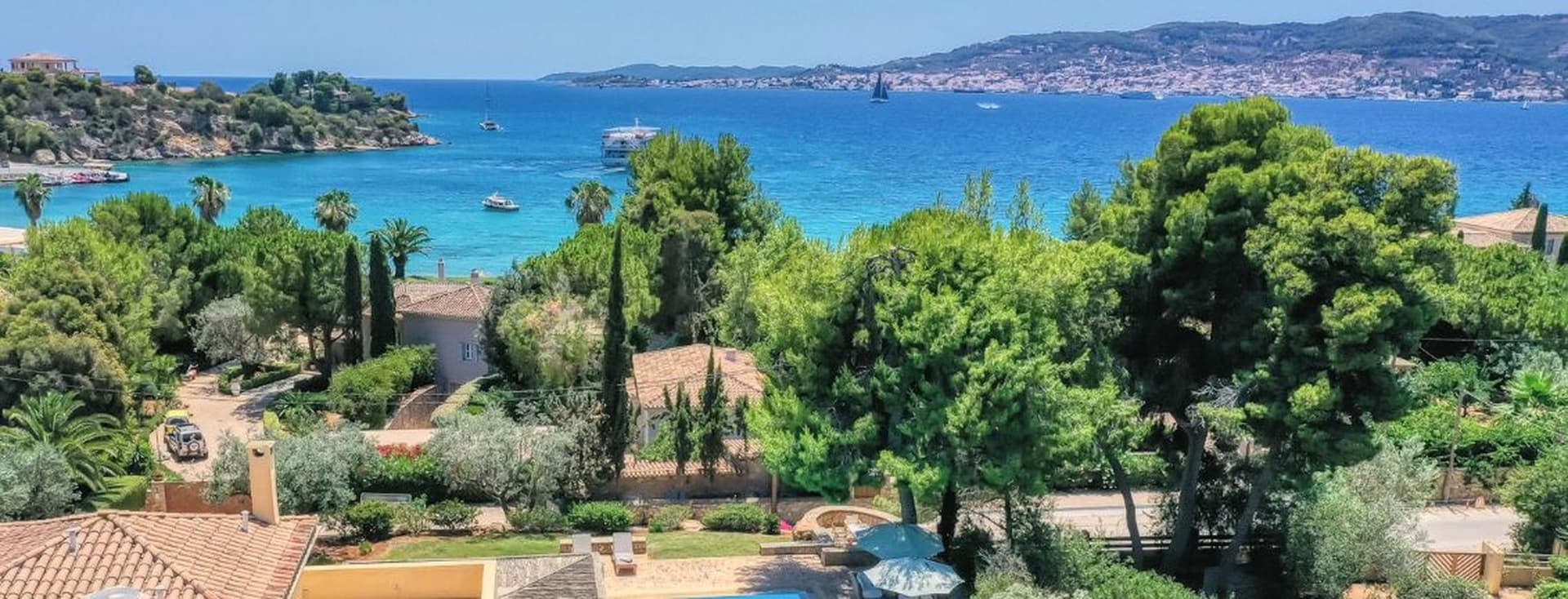 Παραθαλάσσιο τοπίο με τιρκουάζ θάλασσα, πλούσια βλάστηση και σπίτια σε λόφο με θέα στον κόλπο