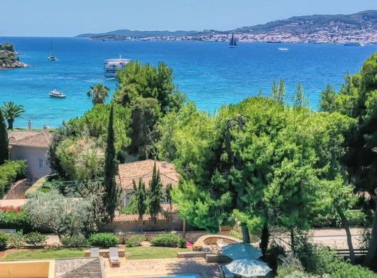 Παραθαλάσσιο τοπίο με τιρκουάζ θάλασσα, πλούσια βλάστηση και σπίτια σε λόφο με θέα στον κόλπο