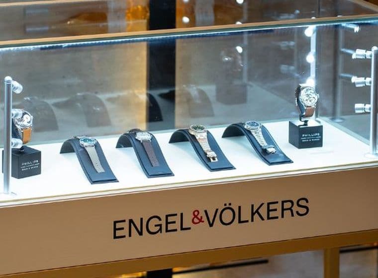 Display case with luxury watches on stands, illuminated under glass. The base is labeled "ENGEL & VÖLKERS."