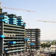 Construction site with several cranes and partially built high-rise buildings against a clear sky.