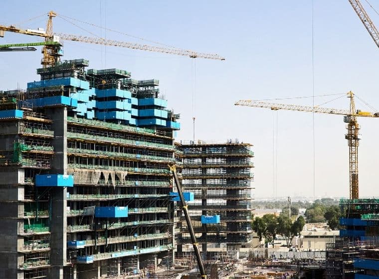 Construction site with several cranes and partially built high-rise buildings against a clear sky.