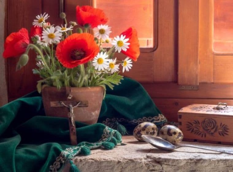 Rustic windowsill still life with red poppies, daisies, green cloth, and wooden music box in warm sunlight.