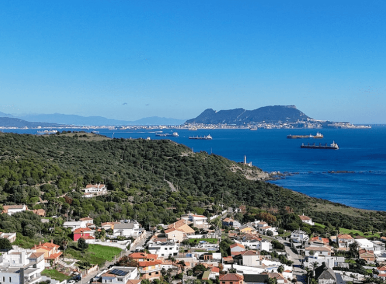 Vistes de l'Estret i Gibraltar des de Punta Carnero. Es veu la ciutat al primer pla de la fotografia i la mar a la dreta amb 6 vaixells de càrrega a l'horitzó.