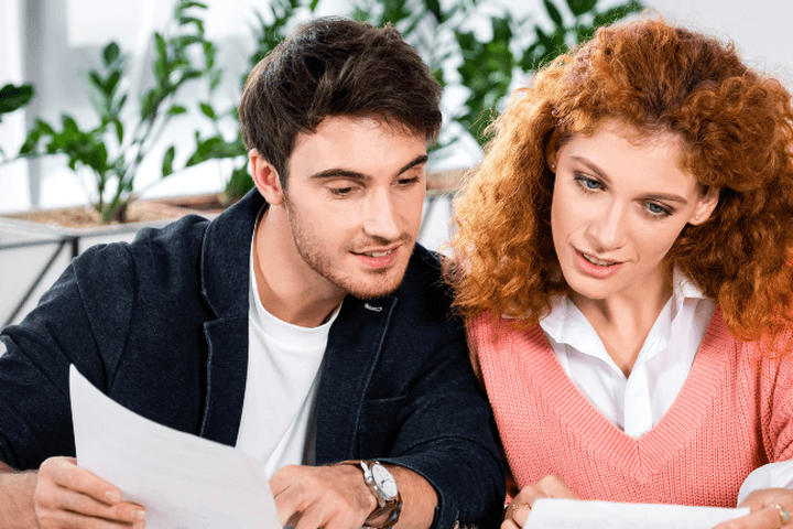 Ein Mann und eine Frau sichten Dokumente an einem Tisch mit Kaffeetassen und Pflanzen.