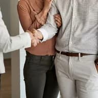Close-up of a couple handshaking with a professional (such as a real estate agent or advisor) in a bright indoor setting.