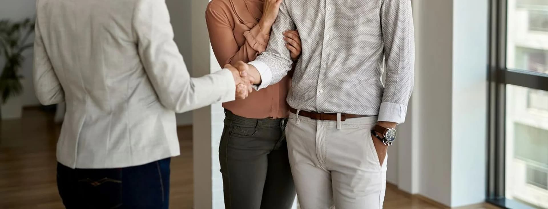 Close-up of a couple handshaking with a professional (such as a real estate agent or advisor) in a bright indoor setting.