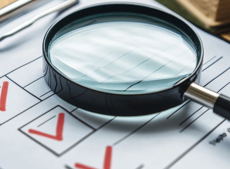 Magnifying glass on a clipboard with a checklist, featuring red checkmarks, resting on a wooden surface.